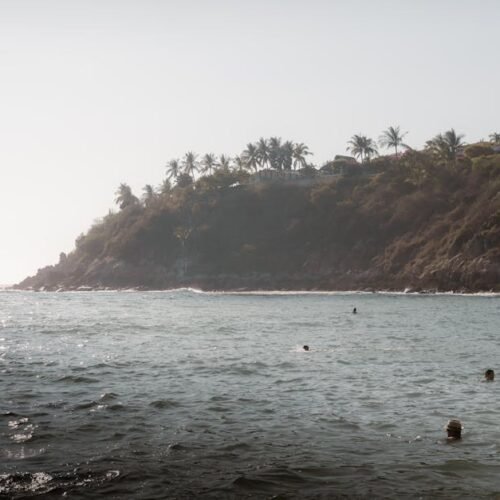 Beach Scenery - Peaceful ocean view with swimmers near a rocky c #15941830